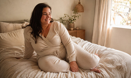 Plus-size woman in cream loungewear relaxing on a bed in warm morning light